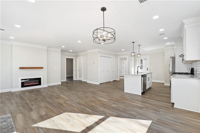 kitchen featuring white cabinetry, hanging light fixtures, stainless steel appliances, ornamental molding, and a center island with sink