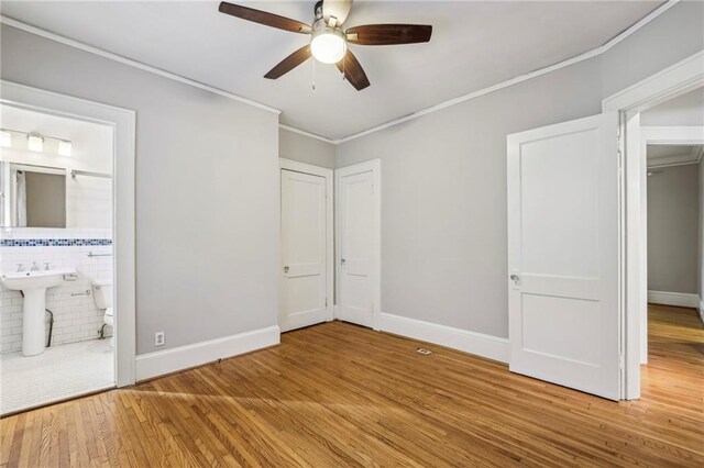 unfurnished bedroom featuring connected bathroom, ceiling fan, wood-type flooring, and ornamental molding