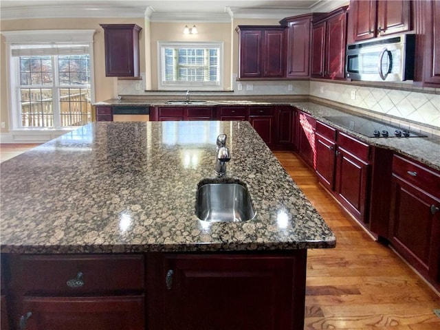 kitchen with a center island with sink, black electric stovetop, dark stone counters, sink, and backsplash