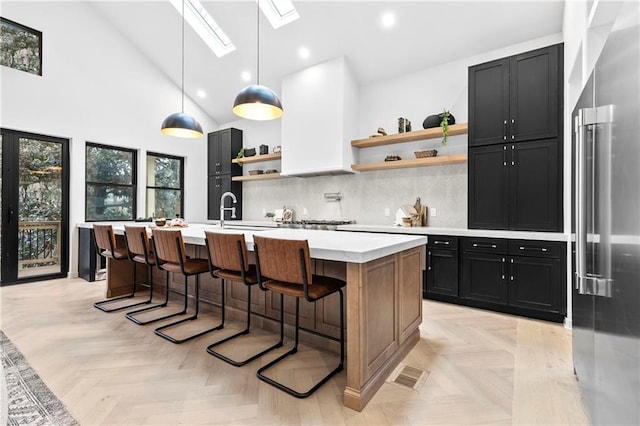 kitchen with an island with sink, high end refrigerator, a kitchen breakfast bar, hanging light fixtures, and light parquet flooring