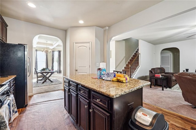 kitchen with dark brown cabinets, a kitchen island, light stone countertops, wood-type flooring, and stainless steel appliances