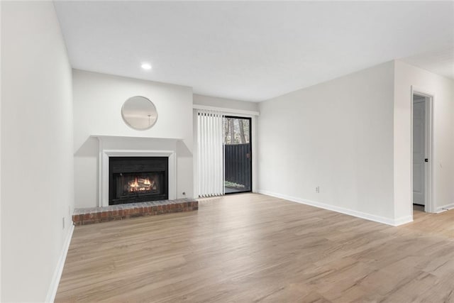 unfurnished living room featuring recessed lighting, a brick fireplace, wood finished floors, and baseboards