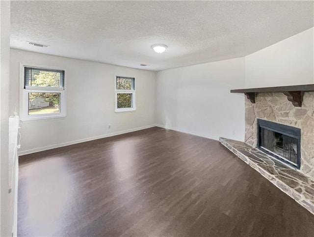 unfurnished living room with dark wood-type flooring, a stone fireplace, a textured ceiling, and plenty of natural light