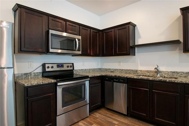 kitchen featuring sink, appliances with stainless steel finishes, dark brown cabinets, dark hardwood / wood-style floors, and light stone counters