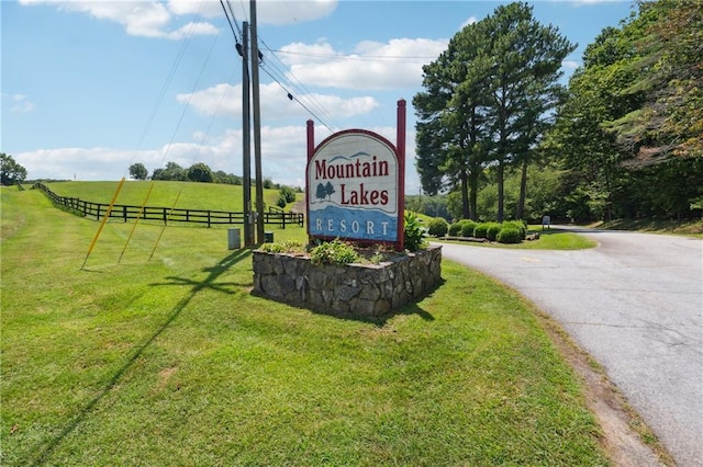 community / neighborhood sign with a lawn, fence, and driveway