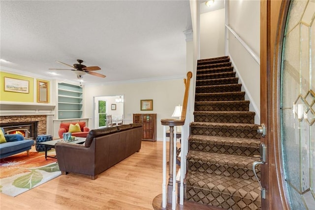 130 Wayne Wheeler Way, Woodstock, GA 30188 - living area with light wood-style flooring, ornamental molding, a ceiling fan, stairs, and a stone fireplace