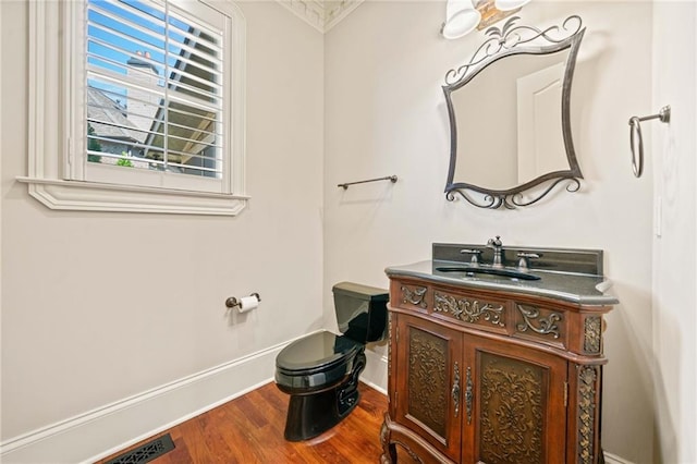 half bath with toilet, wood finished floors, visible vents, vanity, and baseboards