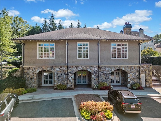 exterior space with french doors, a chimney, a shingled roof, stairway, and stone siding