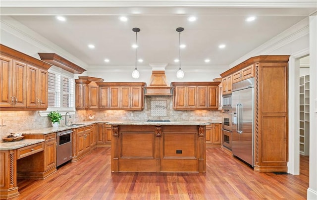 kitchen featuring built in appliances, a kitchen island, a sink, custom exhaust hood, and brown cabinetry