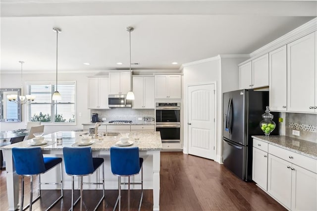 kitchen with stainless steel appliances, white cabinetry, decorative light fixtures, and a kitchen island with sink