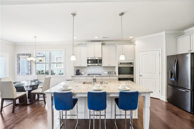 kitchen featuring a center island with sink, stainless steel appliances, hanging light fixtures, light stone counters, and white cabinetry