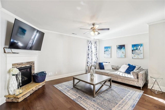 living room with dark wood-type flooring, ceiling fan, crown molding, and a stone fireplace