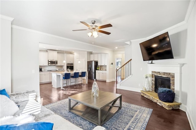 living room featuring ceiling fan, crown molding, dark hardwood / wood-style flooring, and a stone fireplace