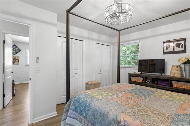 bedroom with an inviting chandelier, baseboards, two closets, and wood finished floors