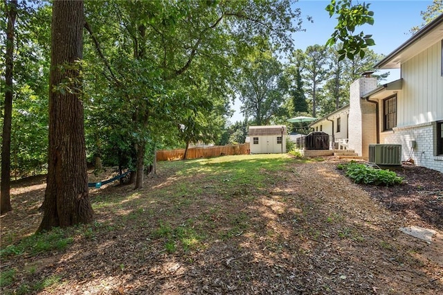 view of yard with central AC, fence, an outdoor structure, and a storage unit