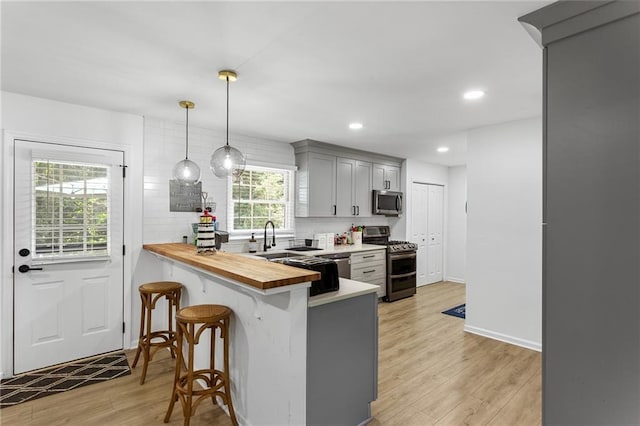kitchen with gray cabinets, a kitchen breakfast bar, butcher block counters, stainless steel appliances, and light wood-style flooring