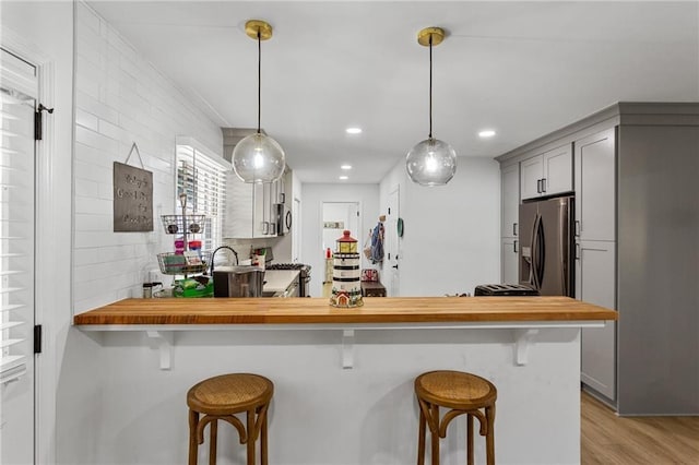 kitchen featuring stainless steel refrigerator with ice dispenser, gray cabinets, a kitchen breakfast bar, and light wood-type flooring