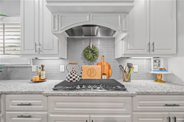 kitchen with stainless steel gas stovetop, light stone counters, backsplash, and white cabinets