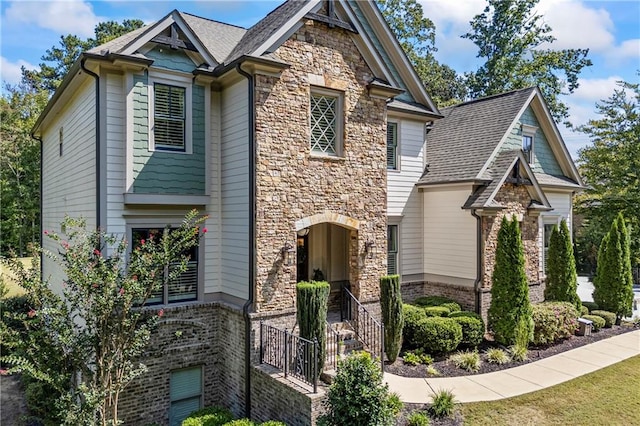 craftsman inspired home featuring stone siding, brick siding, and roof with shingles