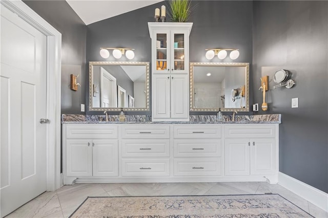 bathroom featuring lofted ceiling, marble finish floor, a sink, and double vanity