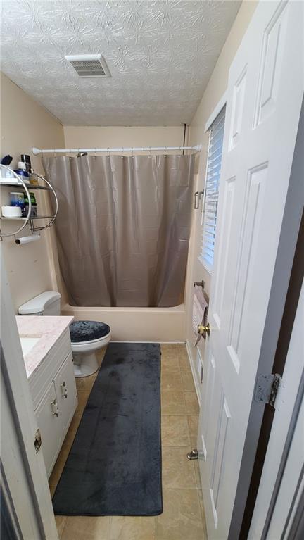 bathroom with visible vents, toilet, shower / bath combo with shower curtain, a textured ceiling, and vanity