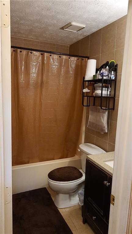 bathroom featuring toilet, tile walls, a textured ceiling, and vanity