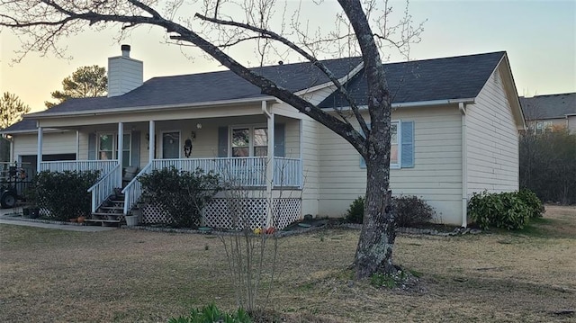 view of front of house with covered porch, a chimney, and a front yard