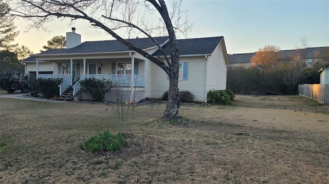 ranch-style home with covered porch, a chimney, fence, and a front lawn