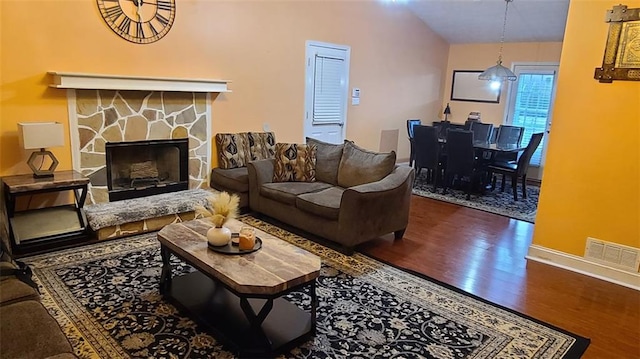 living room with baseboards, visible vents, lofted ceiling, wood finished floors, and a stone fireplace