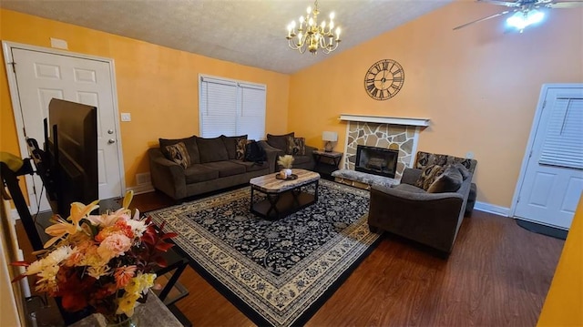 living room with lofted ceiling, a stone fireplace, ceiling fan with notable chandelier, baseboards, and dark wood finished floors