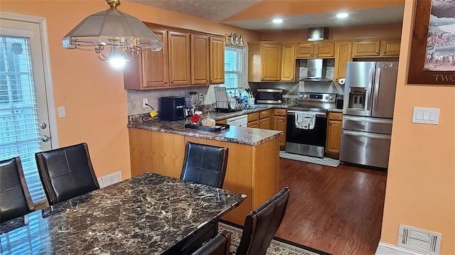 kitchen with dark wood-style floors, decorative light fixtures, stainless steel appliances, visible vents, and exhaust hood