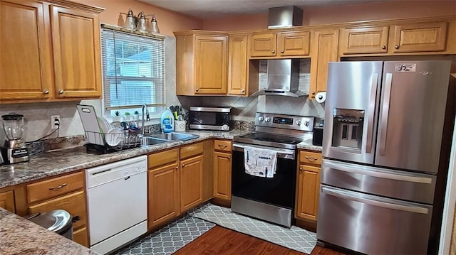 kitchen featuring stone counters, a sink, appliances with stainless steel finishes, wall chimney range hood, and backsplash