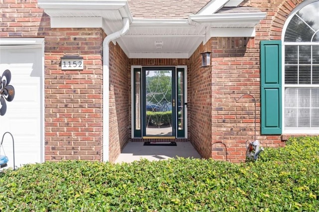 doorway to property featuring a garage, brick siding, and roof with shingles