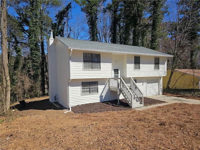 bi-level home with a garage, concrete driveway, and a chimney