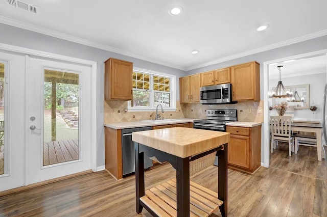 kitchen with appliances with stainless steel finishes, a sink, light wood-style flooring, a chandelier, and ornamental molding
