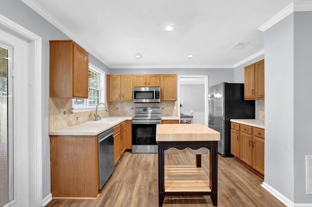 kitchen featuring appliances with stainless steel finishes, a sink, light wood-type flooring, tasteful backsplash, and crown molding
