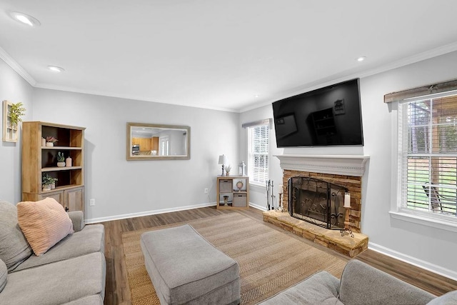 living room with wood finished floors, crown molding, a stone fireplace, baseboards, and recessed lighting