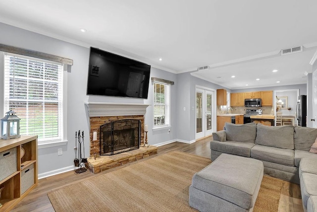 living room with light wood-type flooring, baseboards, crown molding, plenty of natural light, and a stone fireplace