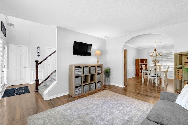 living area with arched walkways, wood finished floors, stairs, a chandelier, and crown molding