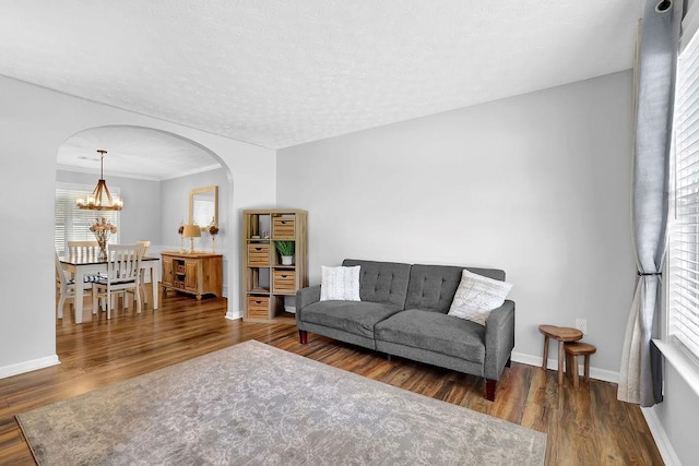 living room with arched walkways, a chandelier, wood finished floors, and baseboards