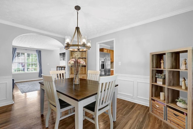 dining area with arched walkways, a chandelier, wainscoting, dark wood-style flooring, and ornamental molding