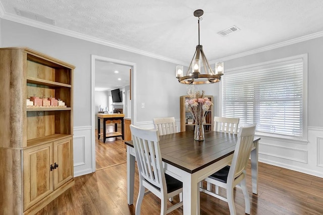 dining area featuring a chandelier, wood finished floors, wainscoting, crown molding, and a decorative wall