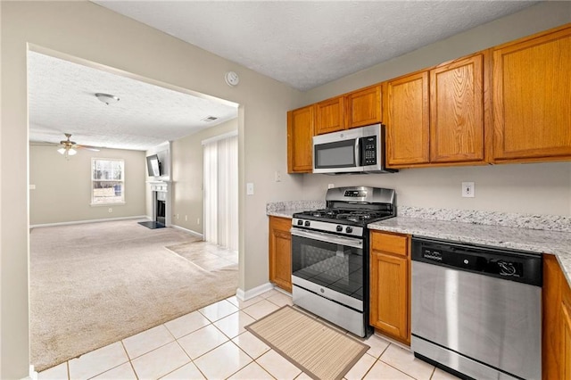 kitchen with a textured ceiling, light carpet, a fireplace, open floor plan, and appliances with stainless steel finishes