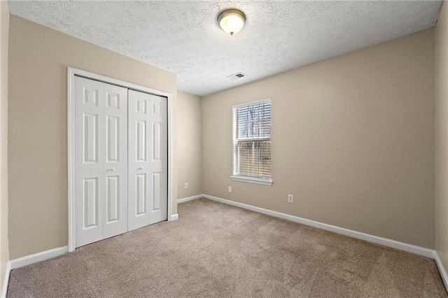 unfurnished bedroom with a textured ceiling, visible vents, baseboards, a closet, and carpet