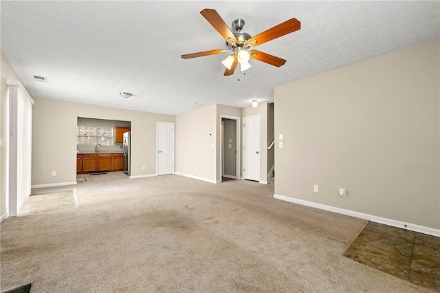 unfurnished living room with light colored carpet, visible vents, a sink, a textured ceiling, and baseboards