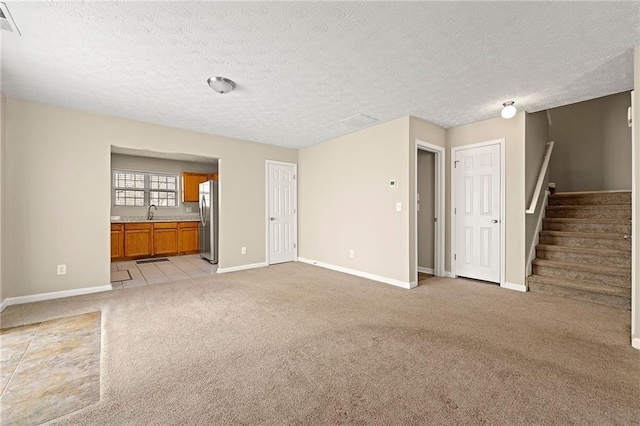 unfurnished living room with light carpet, visible vents, baseboards, stairs, and a textured ceiling