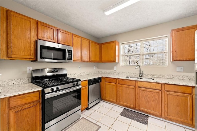 kitchen featuring light tile patterned floors, light stone countertops, stainless steel appliances, a textured ceiling, and a sink