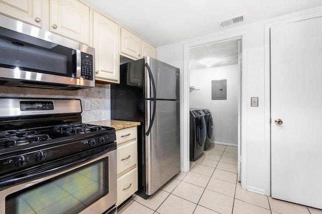 kitchen featuring independent washer and dryer, appliances with stainless steel finishes, light tile patterned floors, light stone countertops, and decorative backsplash