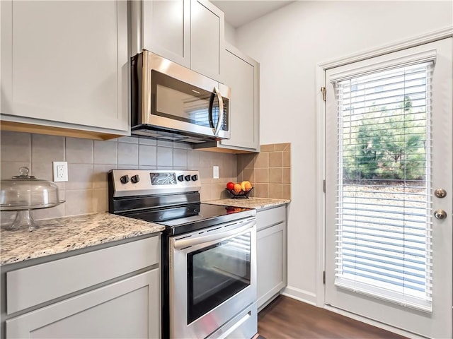 kitchen featuring appliances with stainless steel finishes, a wealth of natural light, light stone countertops, and backsplash