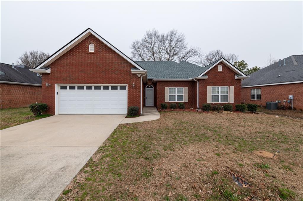 view of front of home with a front yard, central AC, and a garage